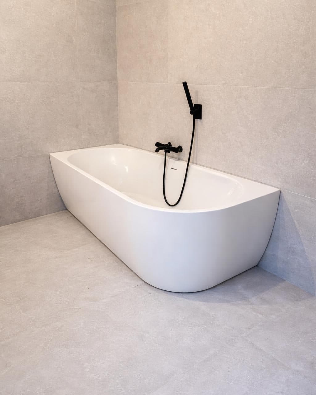 Baignoire d’angle posée contre un carrelage grand format, robinetterie noire
