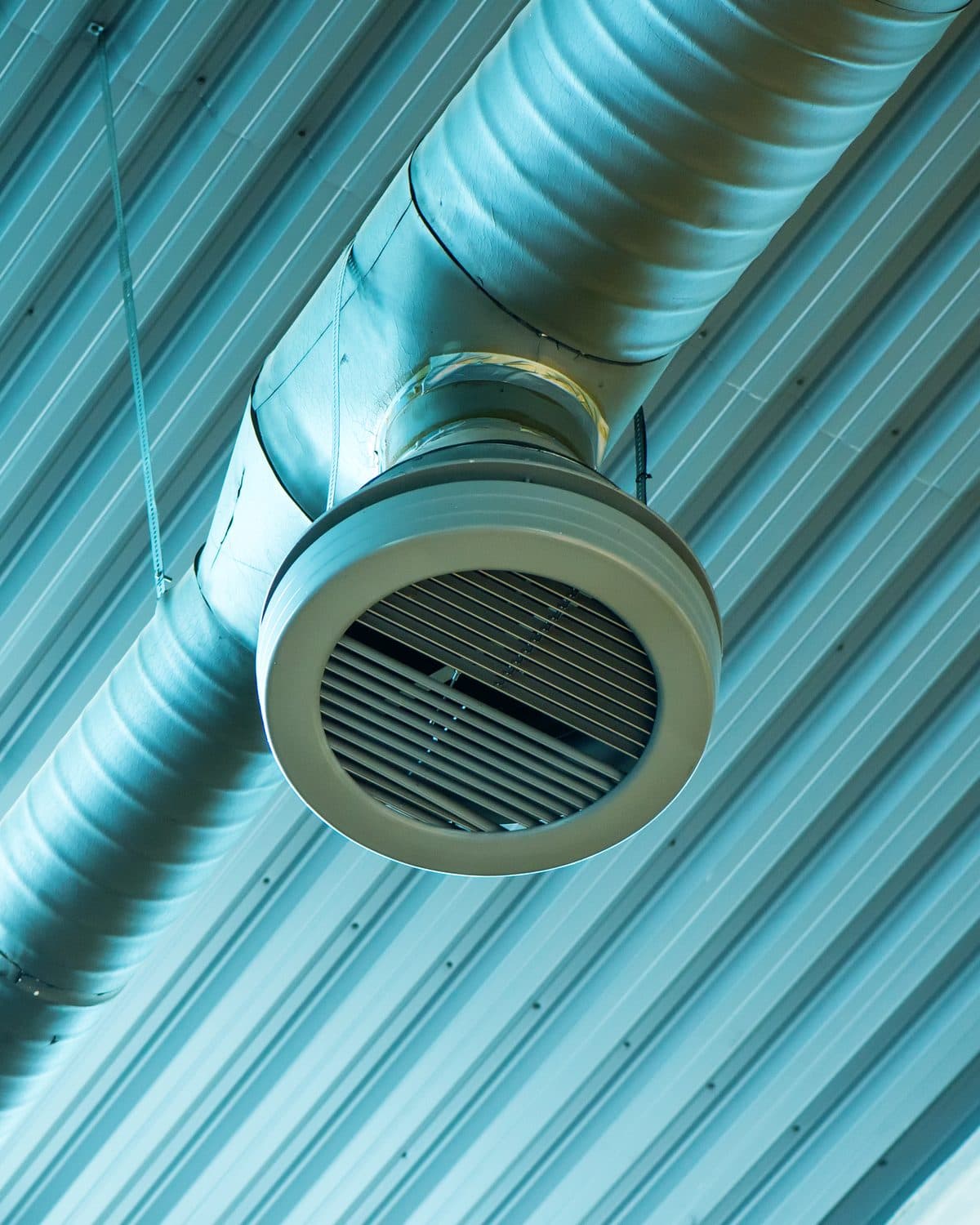 Gaine de ventilation et bouche de soufflage suspendues sous un plafond en tôle